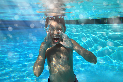 Split shot of little boy playing ball in swimming pool. \nNikon D850