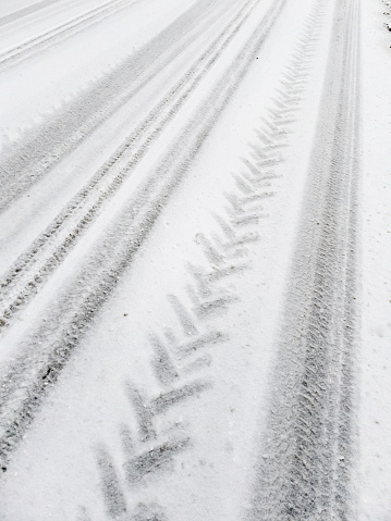 On the snow-covered road tire tracks of cars and the tractor that was cleaning the road.\nThis image was taken with a mobile phone.