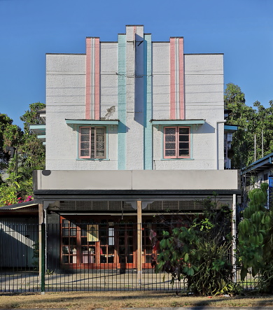 Symmetric facade of AD 1930s erected two story reinforced concrete Art Deco building on Sheridan Str.showing flat parapet of pillar-like decoration painted white-mint-pink. Cairns-Queensland-Australia