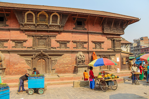 Nepal, Lalitpur - May 10, 2019: Group of street hawkers sells fruits, food and drinks next to wall of Taleju hindu temple on Patan Durbar square in a sunny day. Travel in Nepal theme.