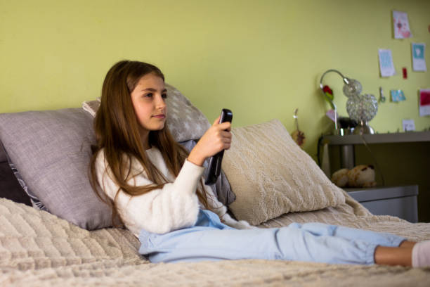 istock Little girl sitting on a sofa and holding a remote control in her hand while watching a cartoon on TV 1461141878