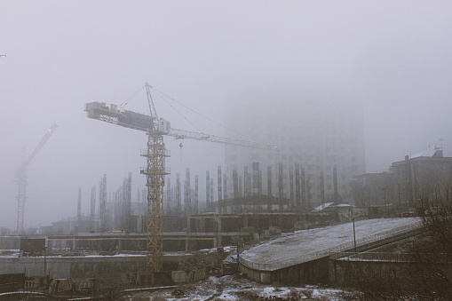 Vintage Style horizontal photo of a construction site with Cranes in Misty Snowy weather