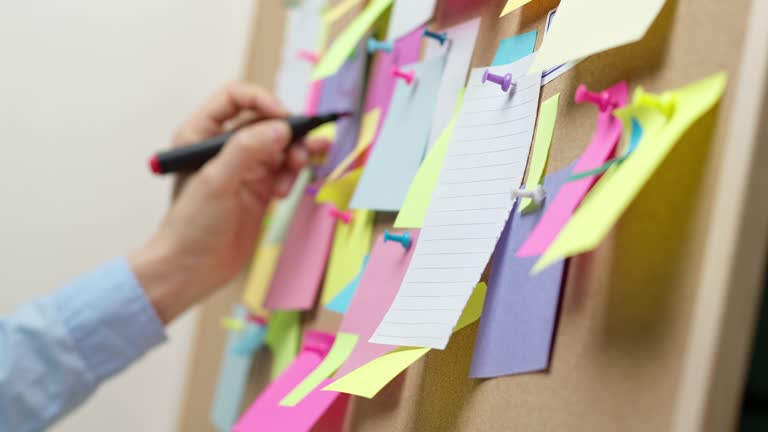 Paper stickers on the visualization board. A woman's hand writes a note. The concept of teamwork, brainstorming.