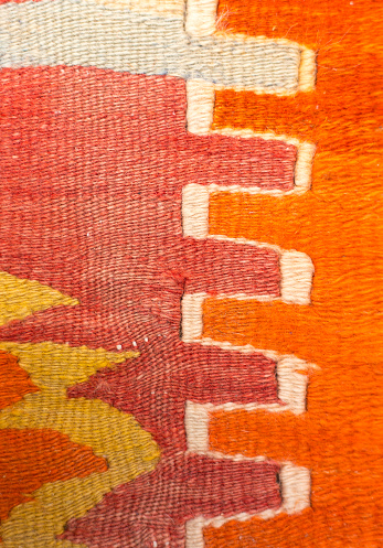 A close-up detail of a vintage wool Turkish kilim rug in orange, yellow and white.