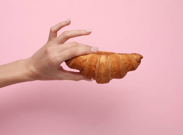 istock Female hand holding a croissant on a pink background 1461156777