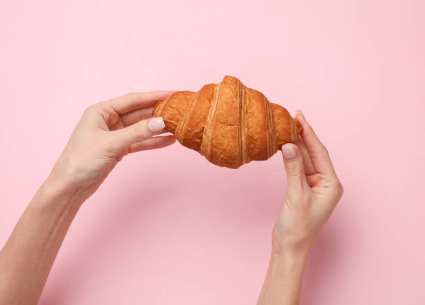 istock Female hands holding a croissant on a pink background 1461156796