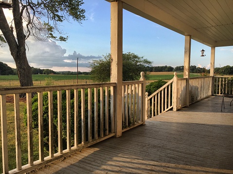 The porch of a farmhouse with a hummingbird feeder and views of surrounding farmland