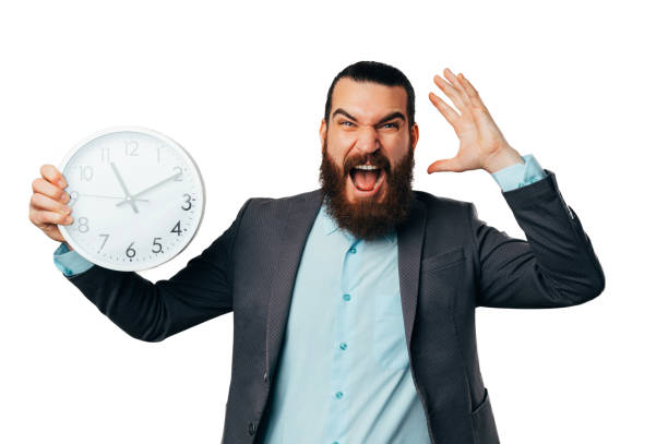 Shocked young bearded man screams load while holding a round white clock. stock photo