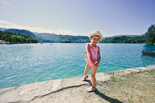 Baby girl is swimsuit and hat posed in pier of view beautiful Bled Lake, Slovenia.