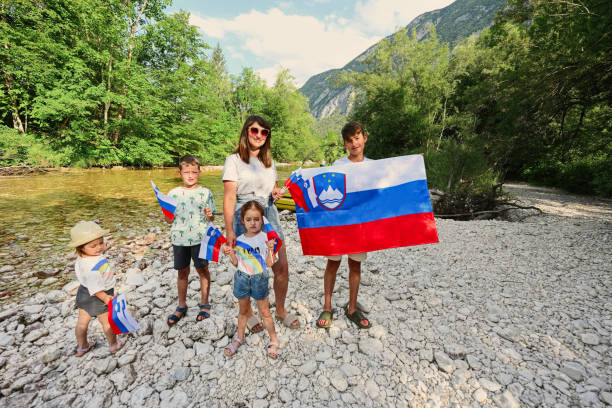 Mother with kids hold slovenian flags in rocky shore of a calm river in Triglav National Park, Slovenia. Mother with kids hold slovenian flags in rocky shore of a calm river in Triglav National Park, Slovenia. фоп 2 група 2022 stock pictures, royalty-free photos & images