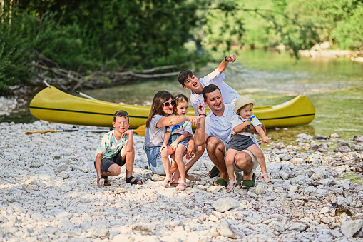 Family with four kids against canoe in rocky shore of a calm river in Triglav National Park, Slovenia.