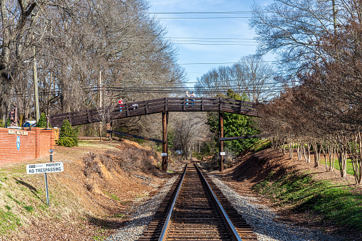 Waxhaw, NC, USA-28 Jan 2023: View down train tracks toward foot bridge, with people pausing on bridge.  Greenery.