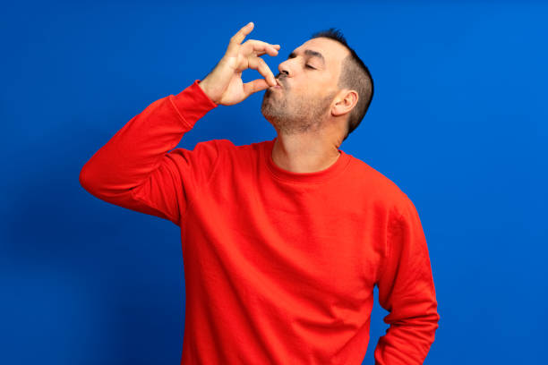 Photo portrait of a man with pursed lips showing gourmet sign with fingers tasty delicious isolated on blue colored background. Photo portrait of a man with pursed lips showing gourmet sign with fingers tasty delicious isolated on blue colored background kiss gesture stock pictures, royalty-free photos & images