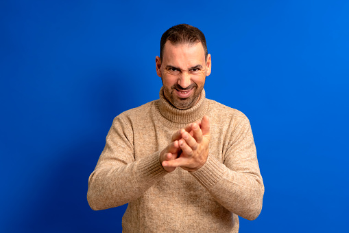 Close-up portrait of cunning, evil, cunning and scheming man, man trying to plot, plan something, screw up, hurt someone, isolated on blue background. Negative human emotions, facial expressions