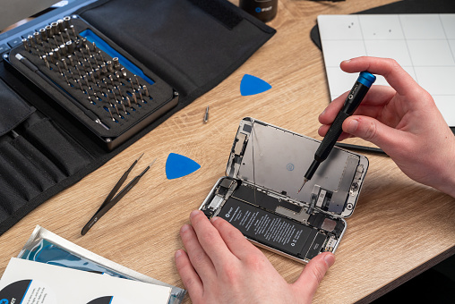 A man performs a self repair on an older iPhone to extend its life, using an iFixit Pro Tech Toolkit and a magnetic project mat. Several opening picks, a pair of precision tweezers, and a precision bit driver is used.