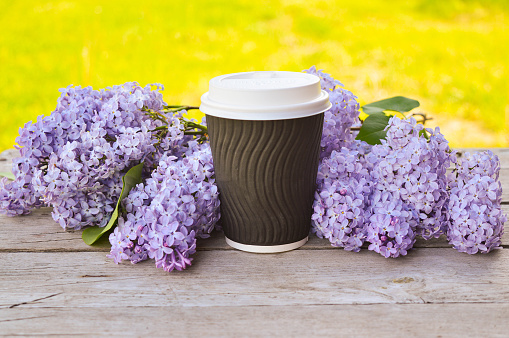 Ecological reusable cup of coffee with lilac flowers on table in street cafe. Coffee and ecology