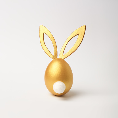 Golden Easter egg with bunny ears and tail on white background. Minimal style, side view. Happy Easter concept.