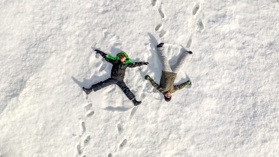 High quality stock photos of two kids playing outside during winter making snow angels.