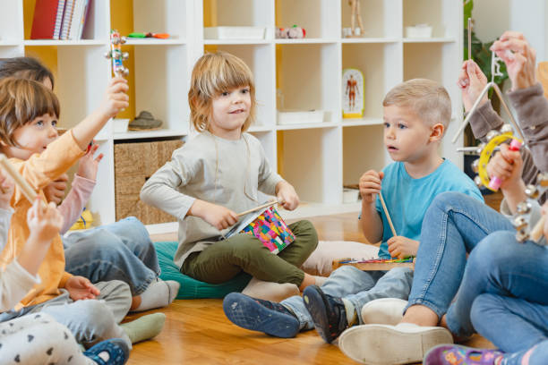 istock Kindergarten teacher with children sitting on the floor having music class, using various instruments and percussion. 1461189156