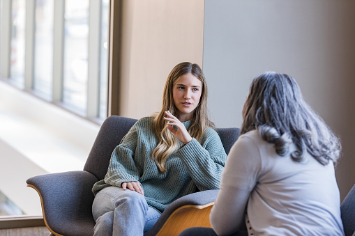 A serious young adult woman gestures as she shares her problems with the unrecognizable senior adult female counselor.