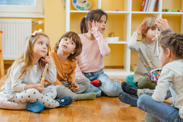 istock Kindergarten teacher with children sitting on the floor having music class, using various instruments and percussion. 1461189389