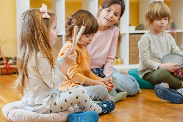 istock Kindergarten teacher with children sitting on the floor having music class, using various instruments and percussion. 1461189490