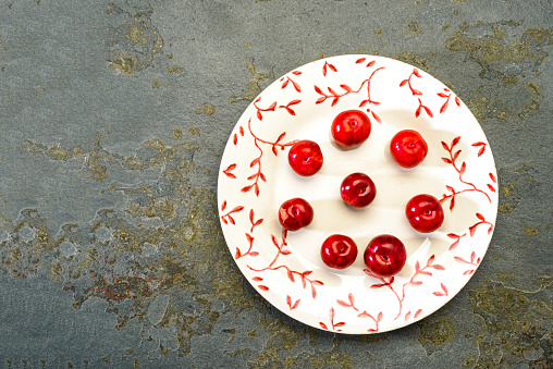 Small plums on white plate on a stone table in the kitchen for snacking as a healthy dessert after lunch or dinner.