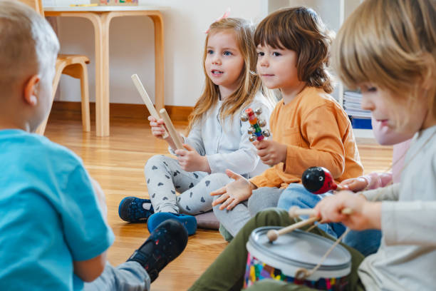 istock Kindergarten teacher with children sitting on the floor having music class, using various instruments and percussion. 1461189533