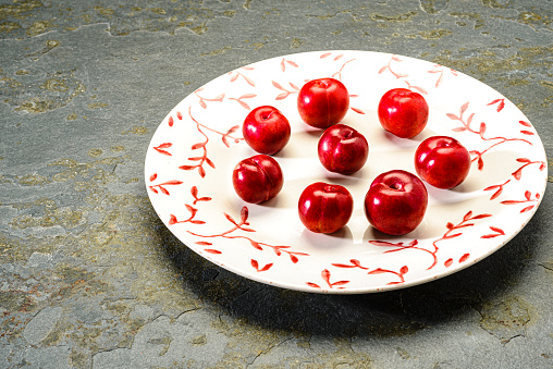 Small plums on white plate on a stone table in the kitchen for snacking as a healthy dessert after lunch or dinner.