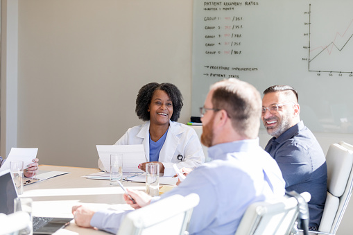 The female surgeon smiles and listens to the guest speaker that is addressing the group today.