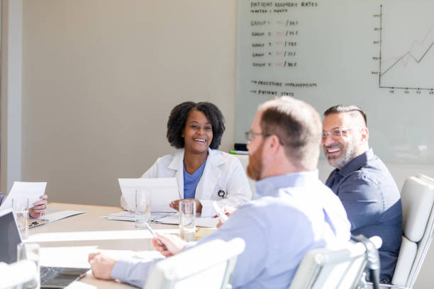 Female surgeon listening to guest speaker The female surgeon smiles and listens to the guest speaker that is addressing the group today. medical insurance data stock pictures, royalty-free photos & images