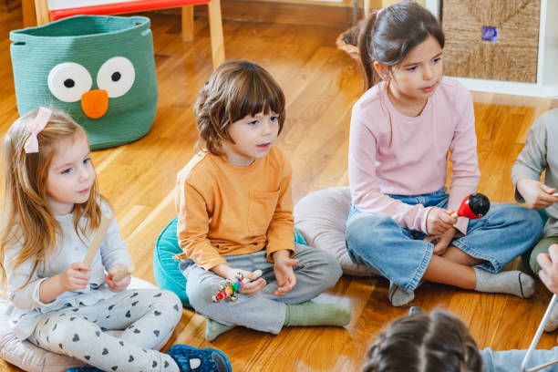 istock Kindergarten teacher with children sitting on the floor having music class, using various instruments and percussion. 1461189906