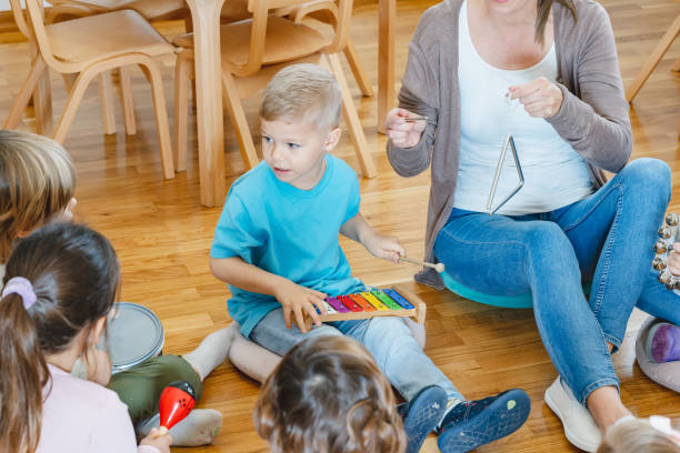 istock Kindergarten teacher with children sitting on the floor having music class, using various instruments and percussion. 1461190019