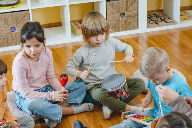 istock Kindergarten teacher with children sitting on the floor having music class, using various instruments and percussion. 1461190693
