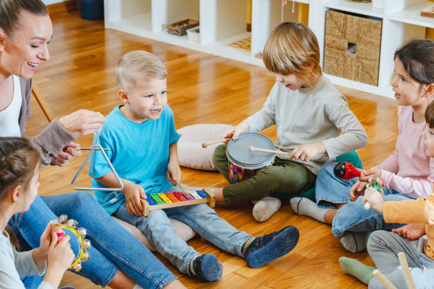 istock Kindergarten teacher with children sitting on the floor having music class, using various instruments and percussion. 1461190711