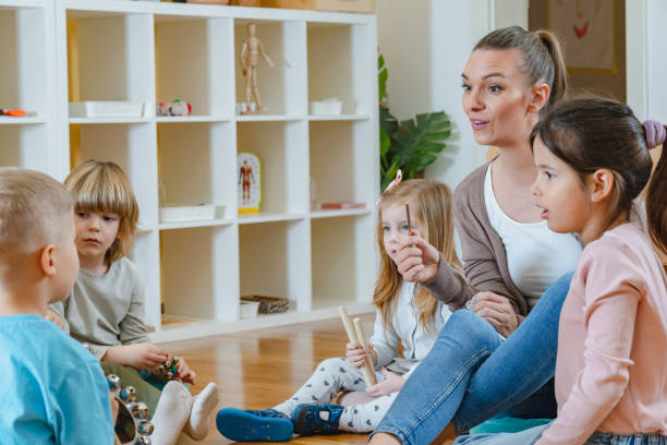 istock Kindergarten teacher with children sitting on the floor having music class, using various instruments and percussion. 1461190721