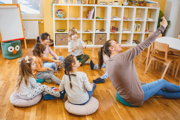 istock Kindergarten teacher with children sitting on the floor having music class, using various instruments and percussion. 1461190886