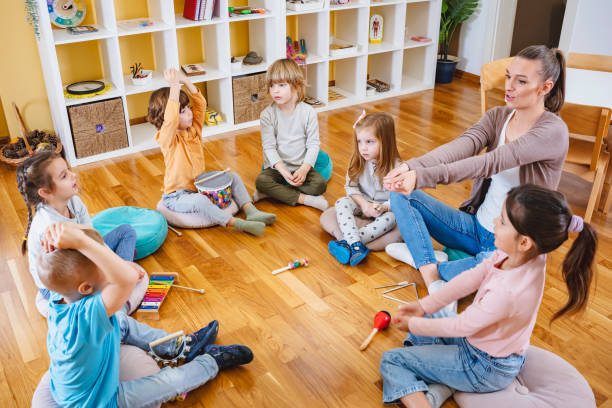 istock Kindergarten teacher with children sitting on the floor having music class, using various instruments and percussion. 1461190907
