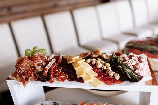 Mix of different snacks and appetizers. Tapas bar. Ham, sausage, cheese, jamon, salami, grape, figs and rosemary on white plate on corporate christmas birthday party event or wedding celebration.