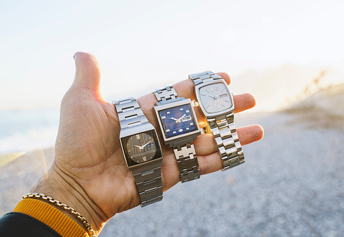 Hand holding three different type of vintage watches on the beach