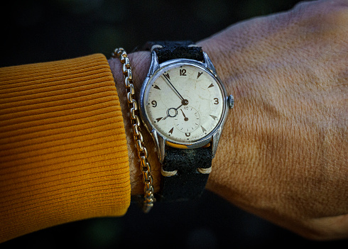 Vintage wrist watch and gold bracelet on man's arm, close up
