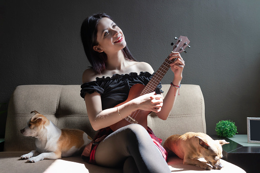 Young girl playing ukulele with her puppies as listeners