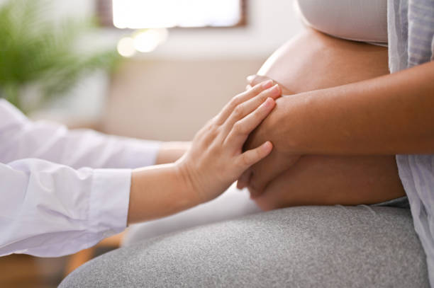 Side view of a doctor touching a pregnant woman's belly, feeling the baby inside the tummy. stock photo