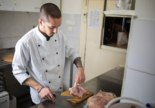 A young male cook is cutting pork and preparing it for roasting in the kitchen of a local restaurant