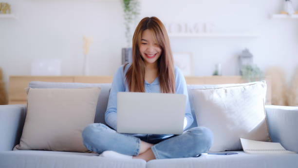 istock Young asian woman using laptop while seated on couch at home 1461212705