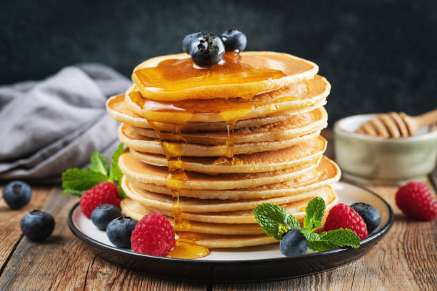 istock Delicious pancakes, with fresh blueberries, raspberry and maple syrup or honey on a dark background 1461214637