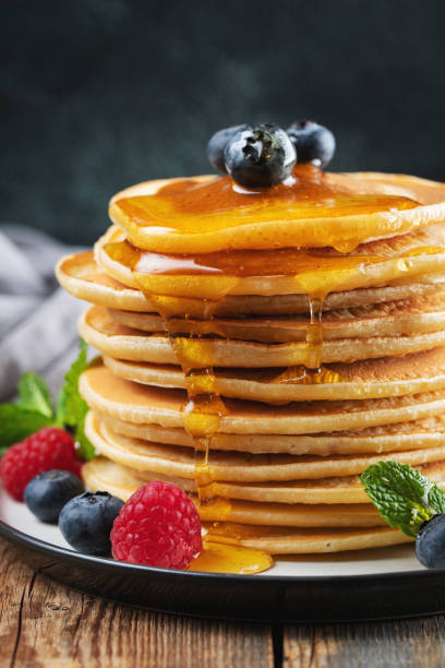 istock Delicious pancakes, with fresh blueberries, raspberry and maple syrup or honey on a dark background 1461214684