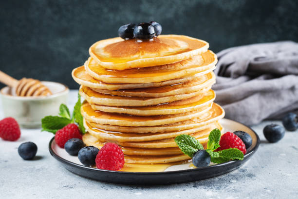 istock Delicious pancakes, with fresh blueberries, raspberry and maple syrup or honey on a dark background 1461214853