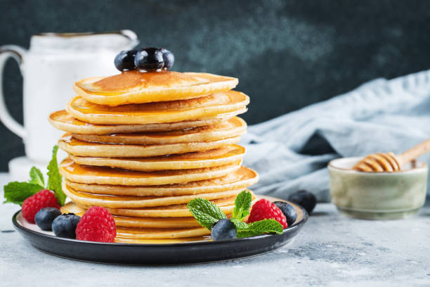 istock Delicious pancakes, with fresh blueberries, raspberry and maple syrup or honey on a dark background 1461214955