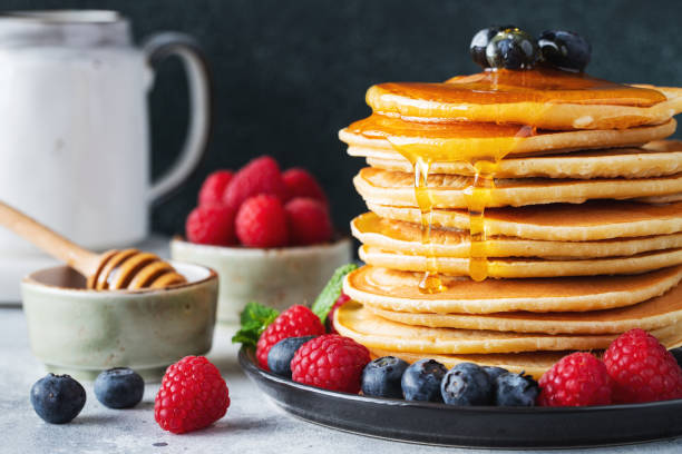 istock Delicious pancakes, with fresh blueberries, raspberry and maple syrup or honey on a dark background 1461214965